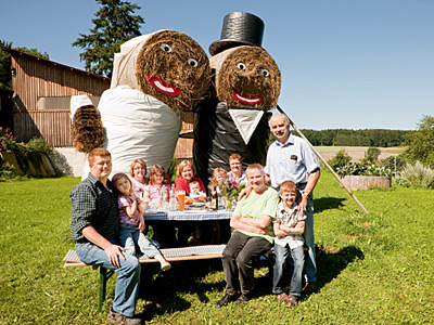 Betriebsleiter mit Familie und Eltern vor überlebensgroßen Figuren aus Strohballen